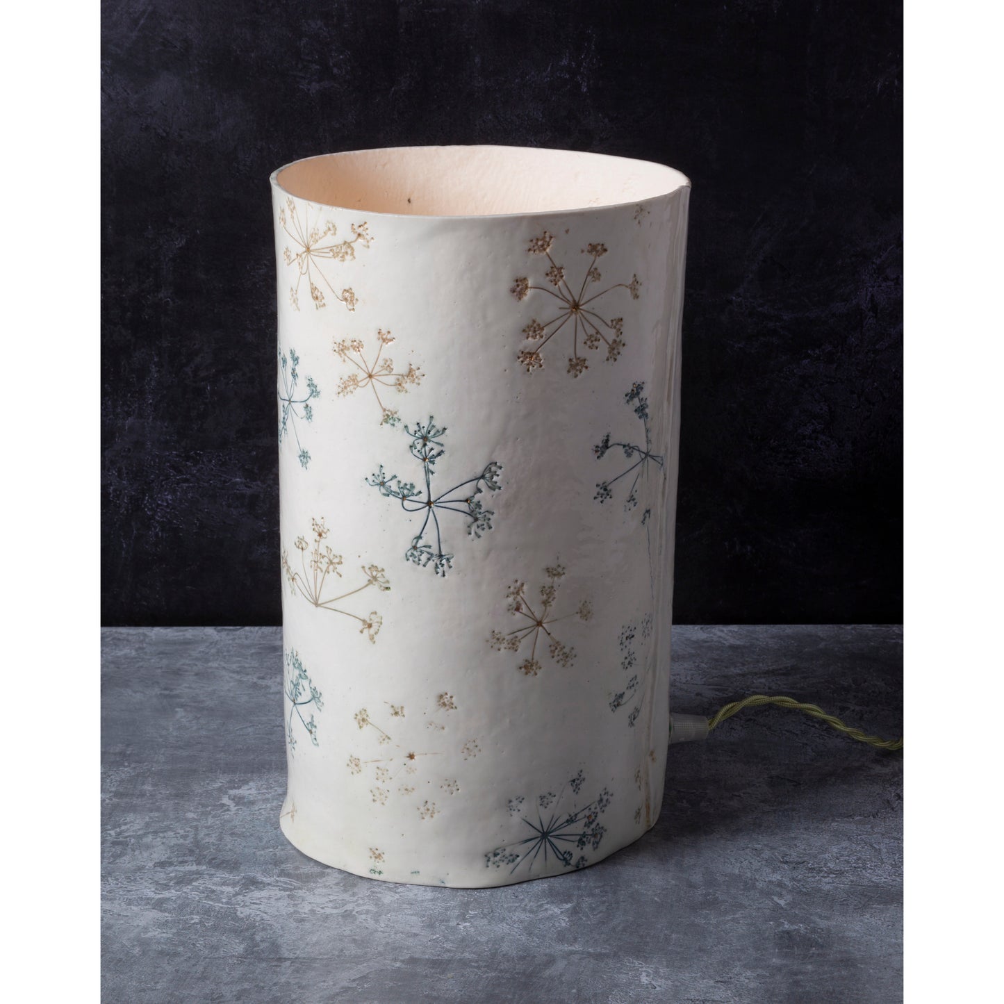 White cylindrical lamp unlit with floral patterns on a dark background