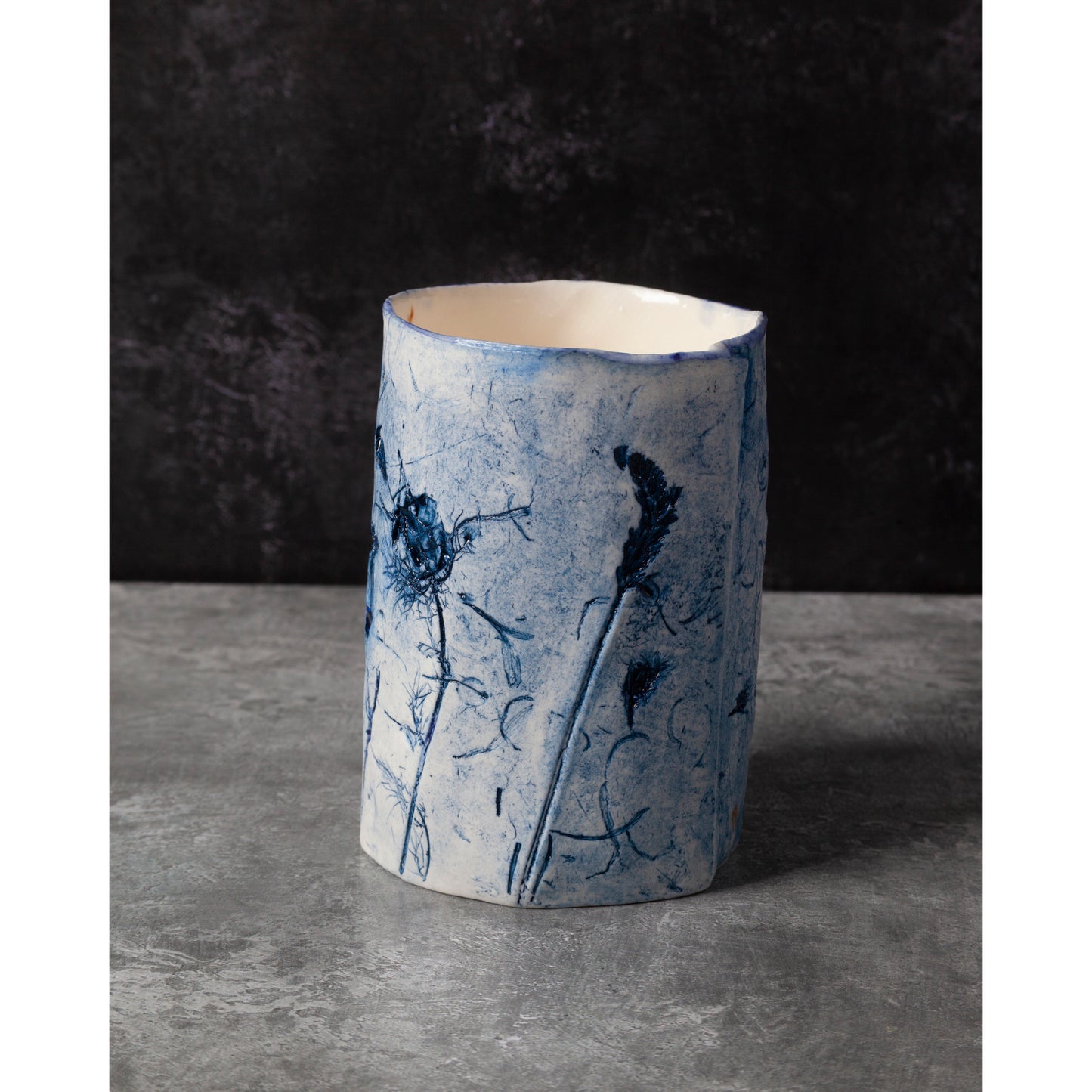 Cylindrical ceramic vase with blue floral patterns on a dark background