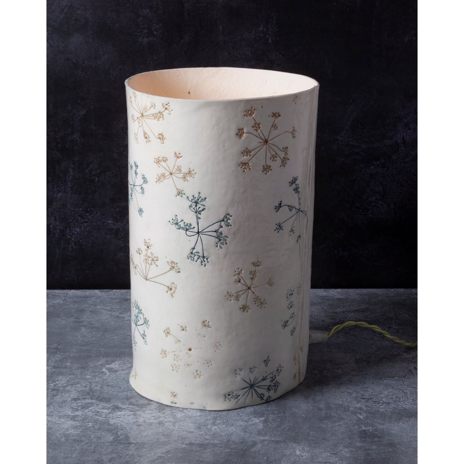 White cylindrical lamp unlit with floral patterns on a dark background