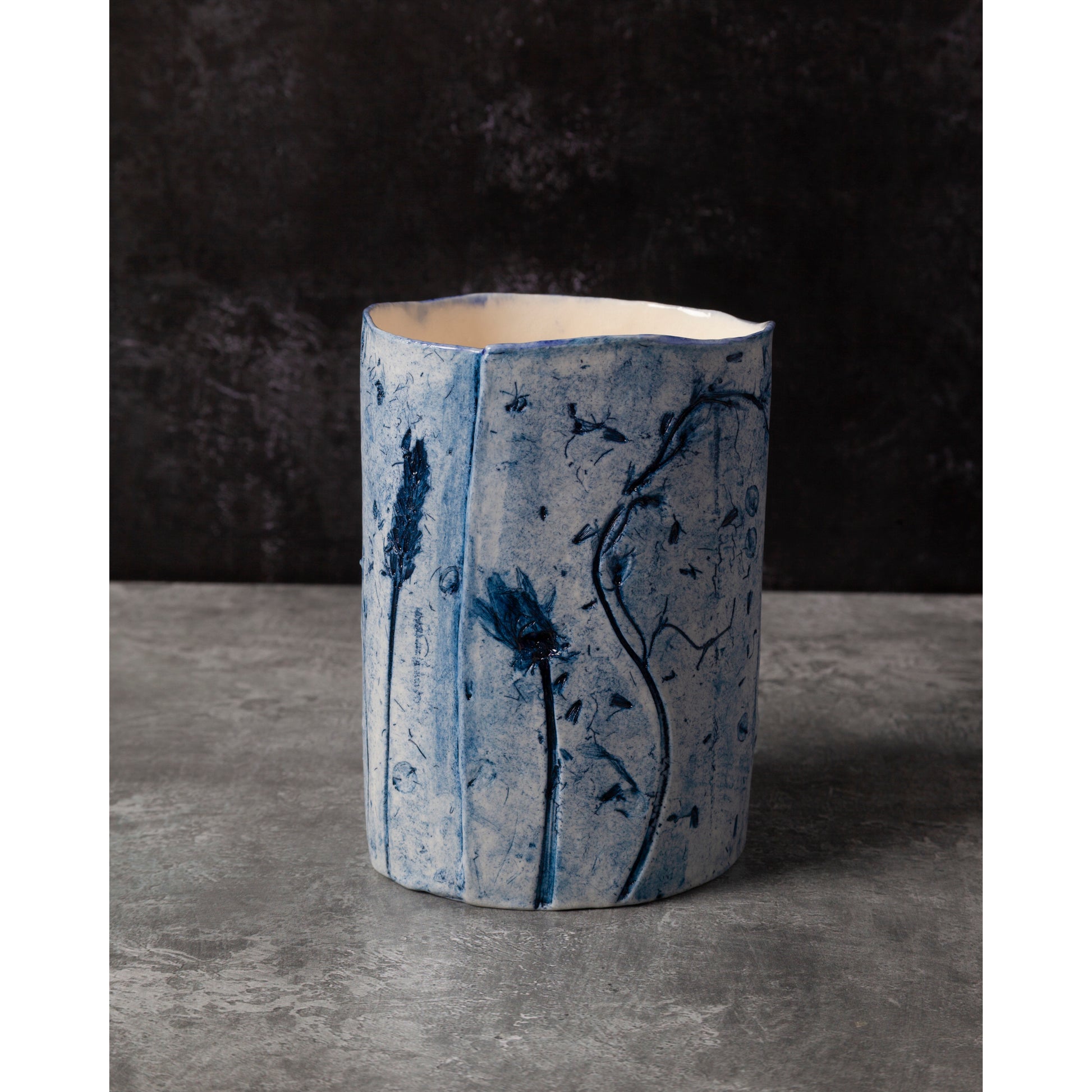 Cylindrical ceramic vase with blue floral patterns on a dark background