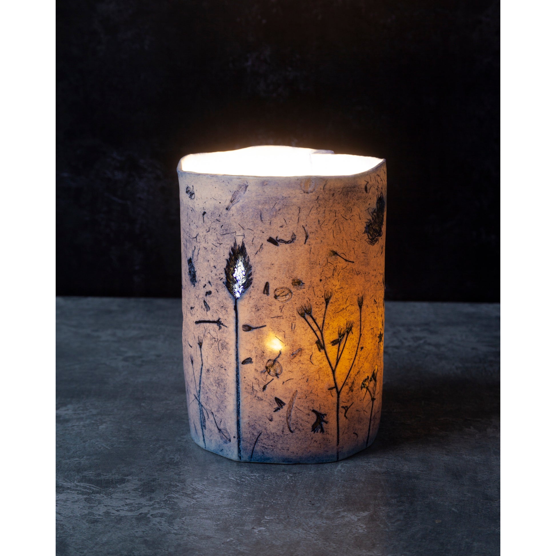 Cylindrical candle holder with floral patterns on a dark background