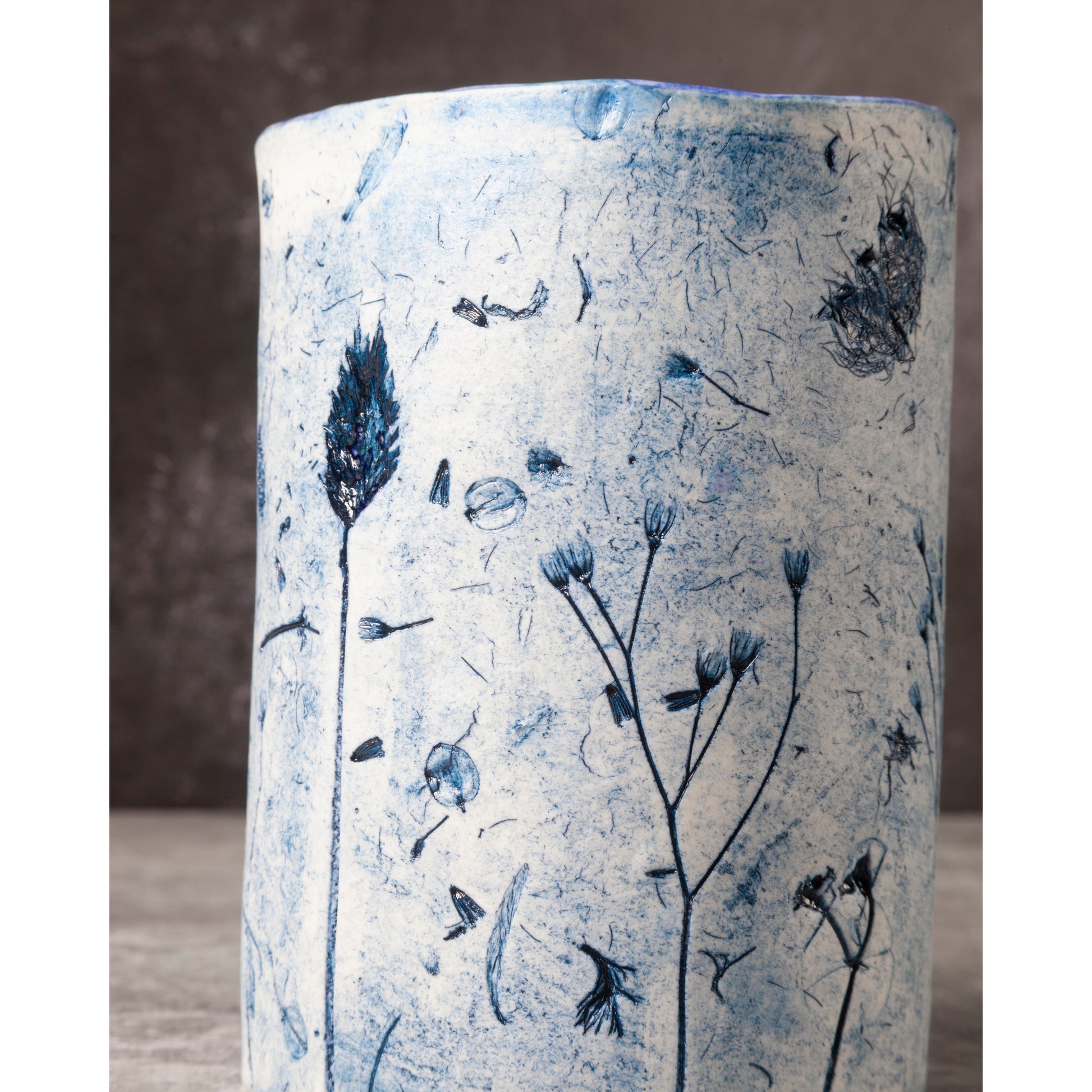 Cylindrical ceramic vase with blue botanical patterns on a textured surface