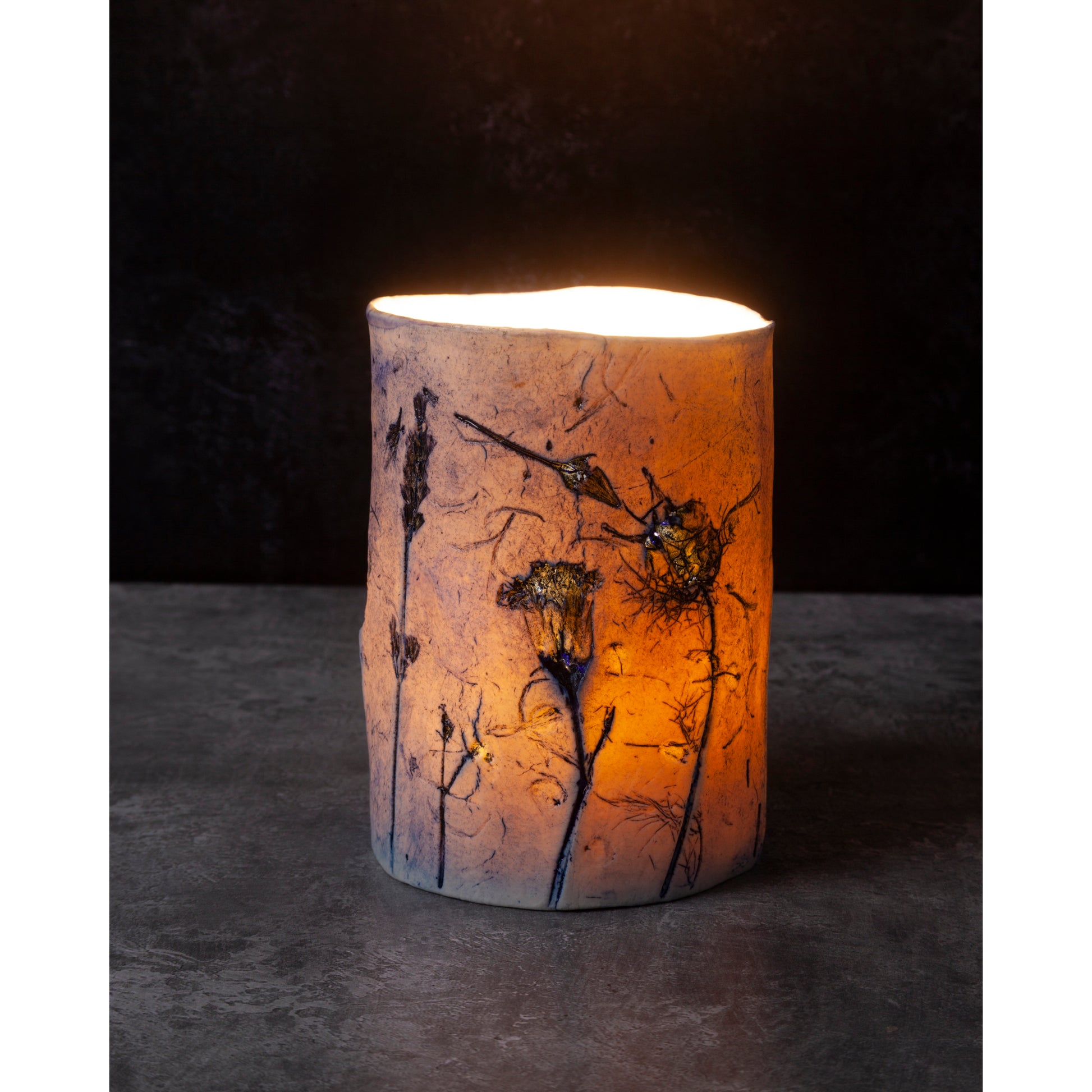 Cylindrical candle holder with floral design on a dark background
