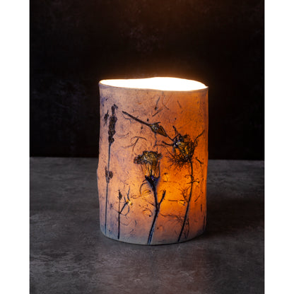 Cylindrical candle holder with floral design on a dark background
