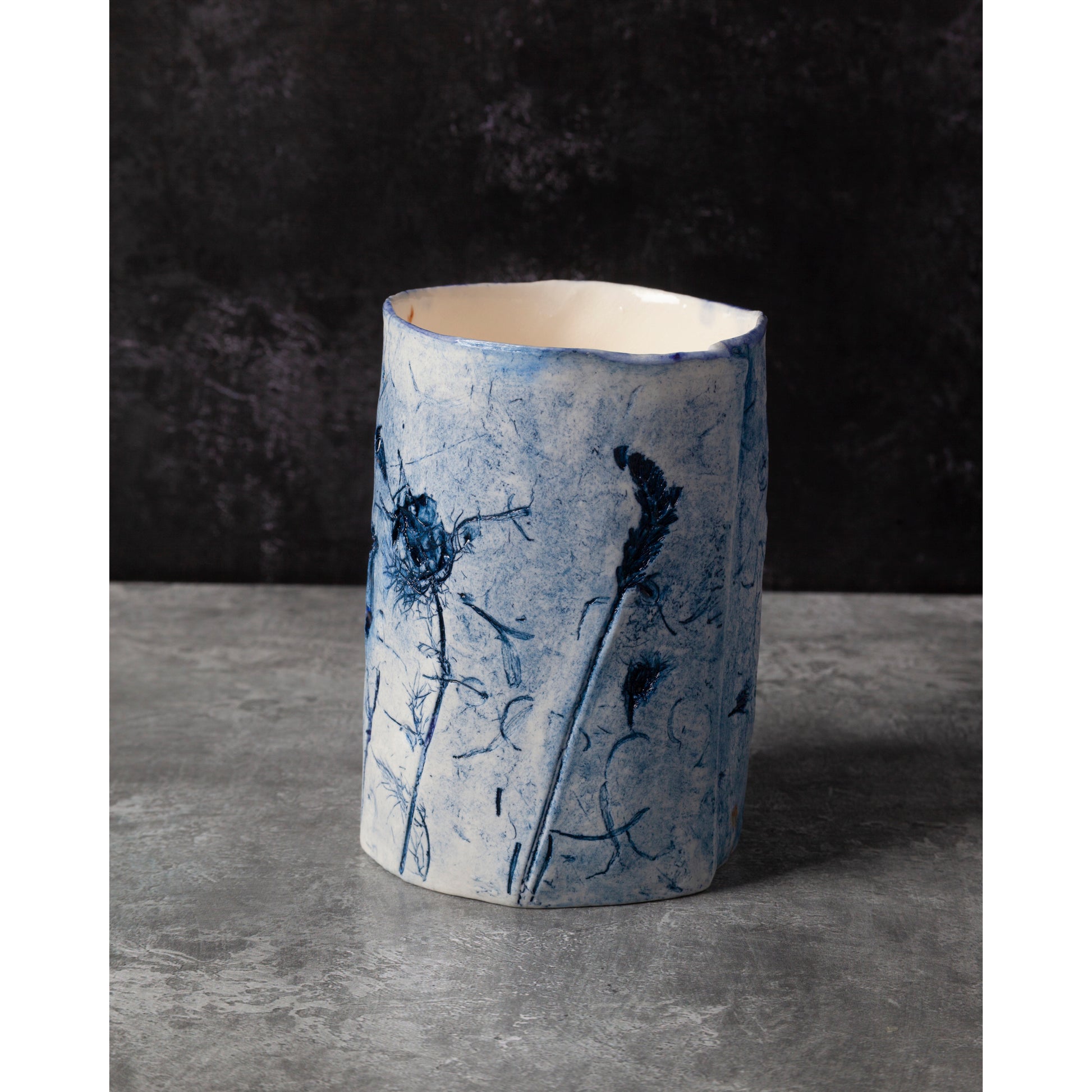 Cylindrical ceramic vase with blue floral patterns on a dark background