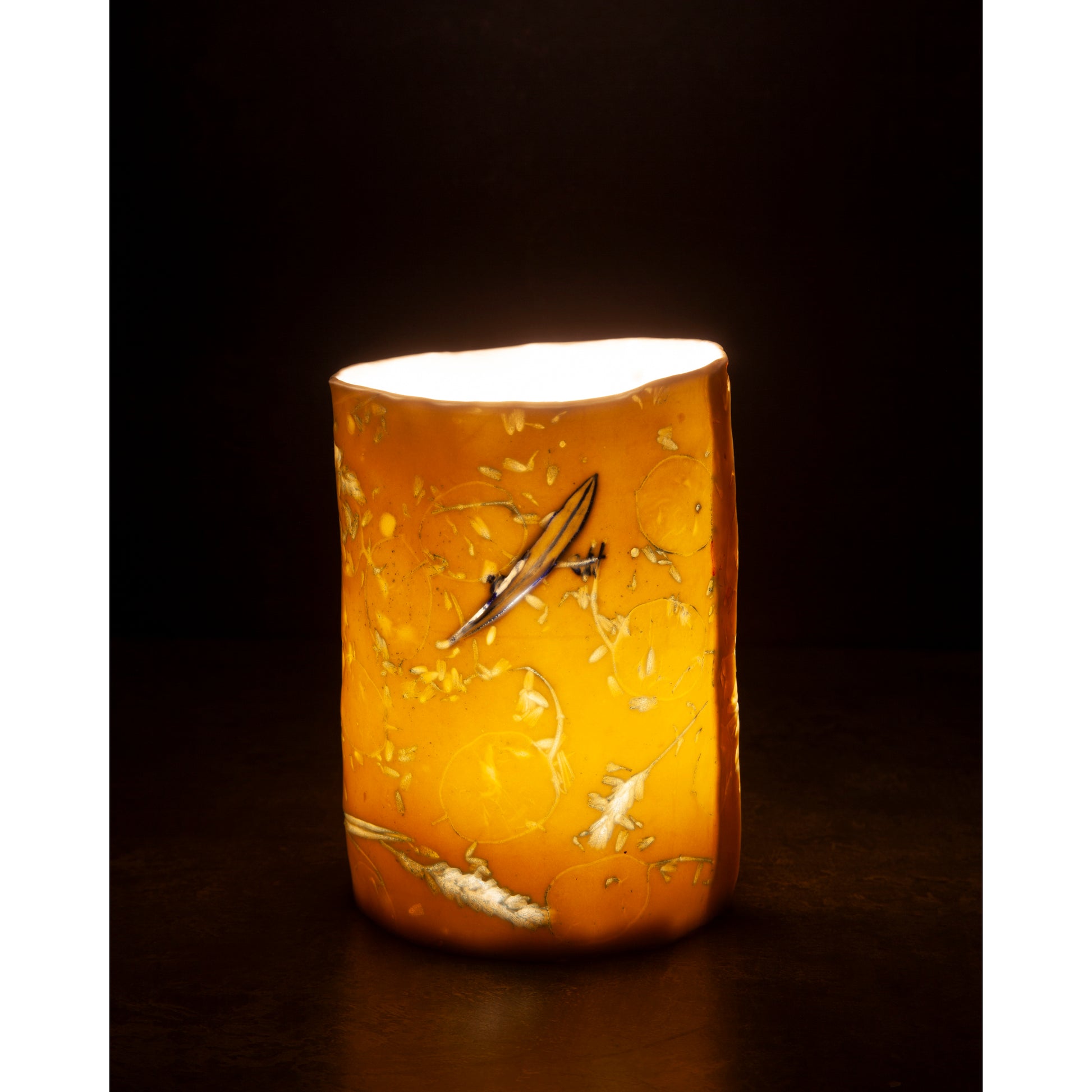 Cylindrical porcelain night light / vase with abstract designs  using honesty seed heads, lavender, grasses and olive leaves photographed in a dark background