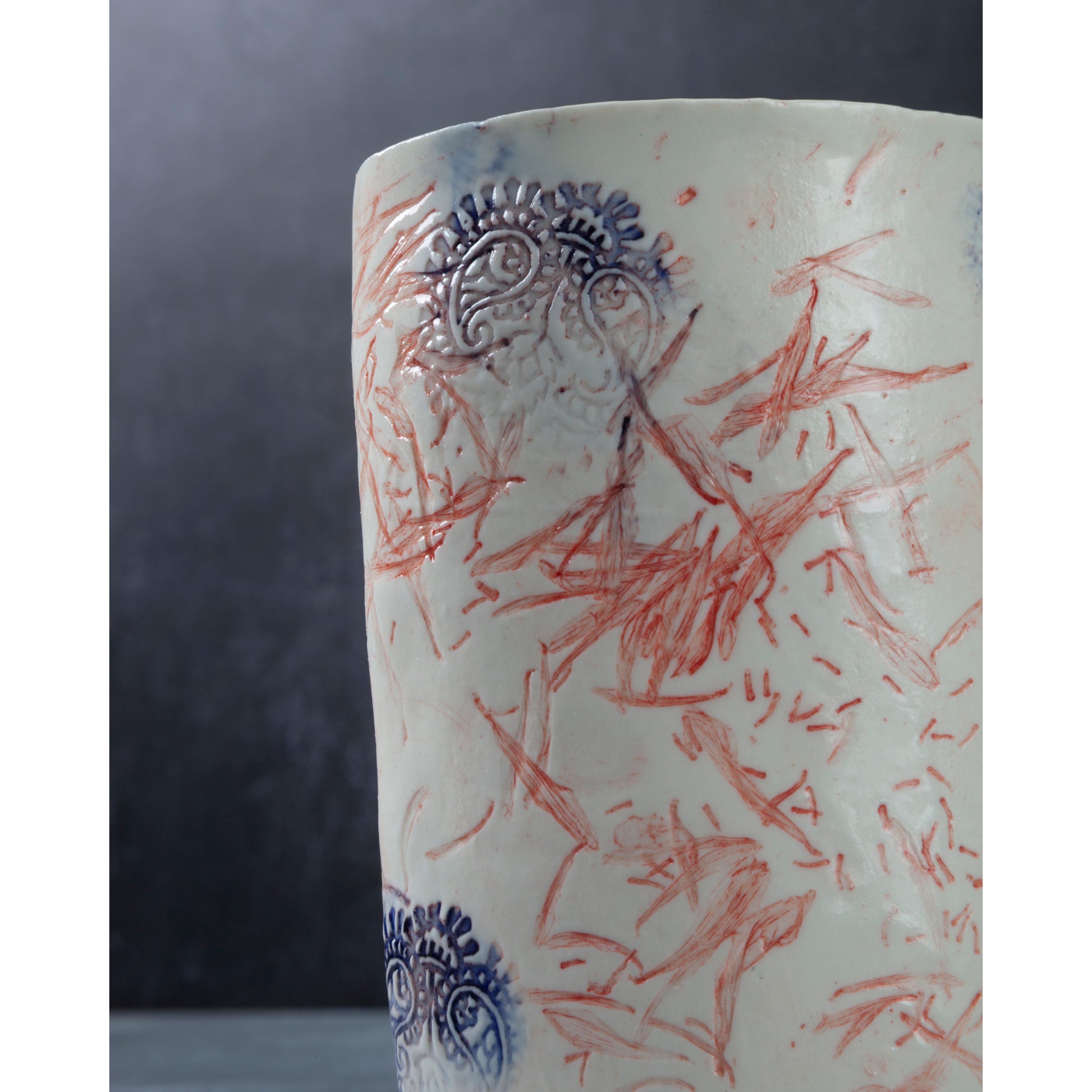 Detail of Ceramic vase with red and blue floral patterns and Indian wood block decorative elements. Photographed on a dark background