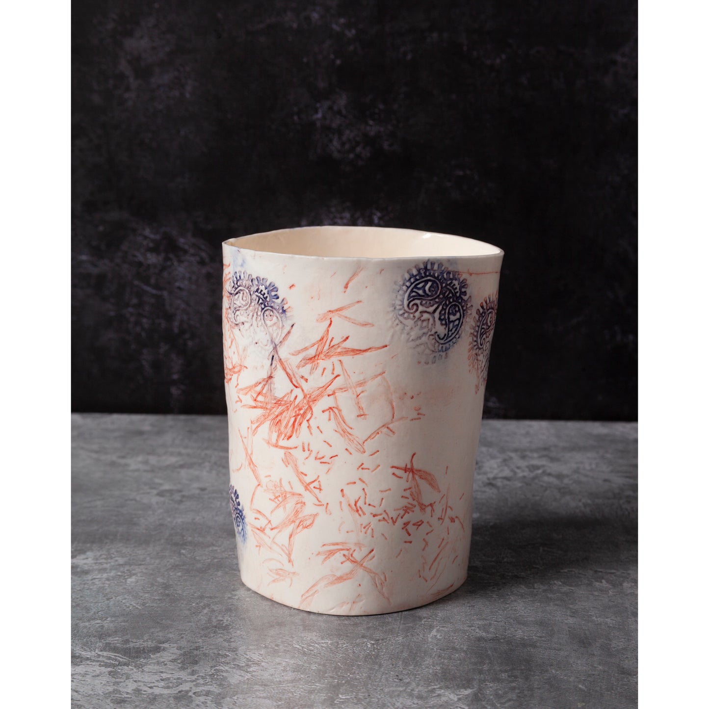 Ceramic tealight - vase with red and blue floral patterns and Indian wood block decorative elements. Photographed on a dark background