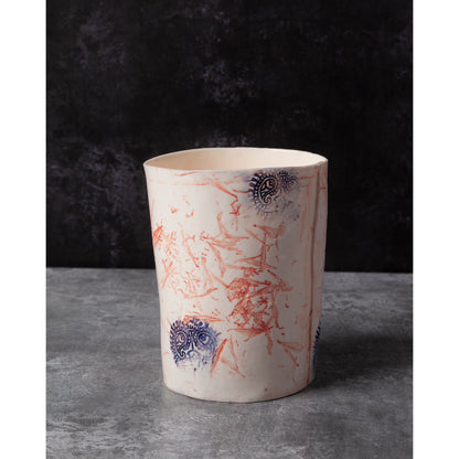 Porcelain vase with red and blue floral patterns and Indian wood block decorative elements. Photographed on a dark background