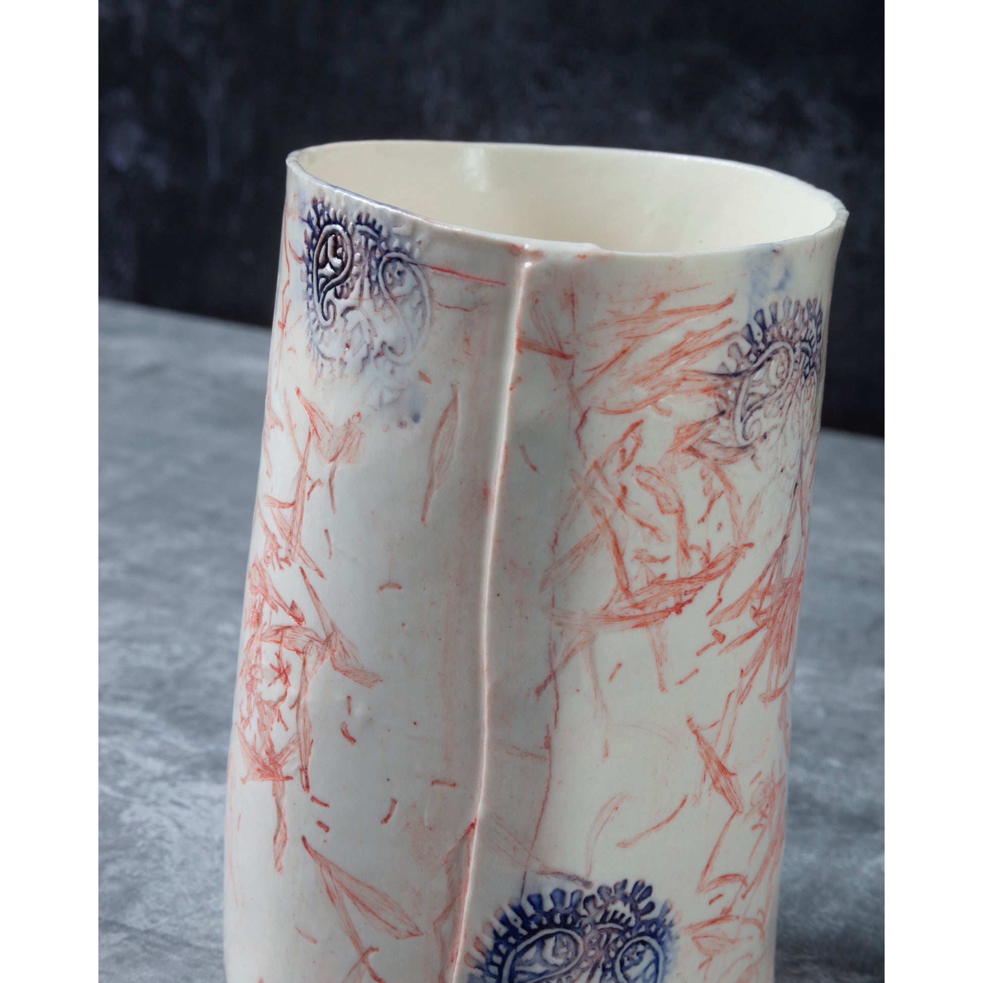 Detail of Ceramic vase with red and blue floral patterns and Indian wood block decorative elements. Photographed on a dark background