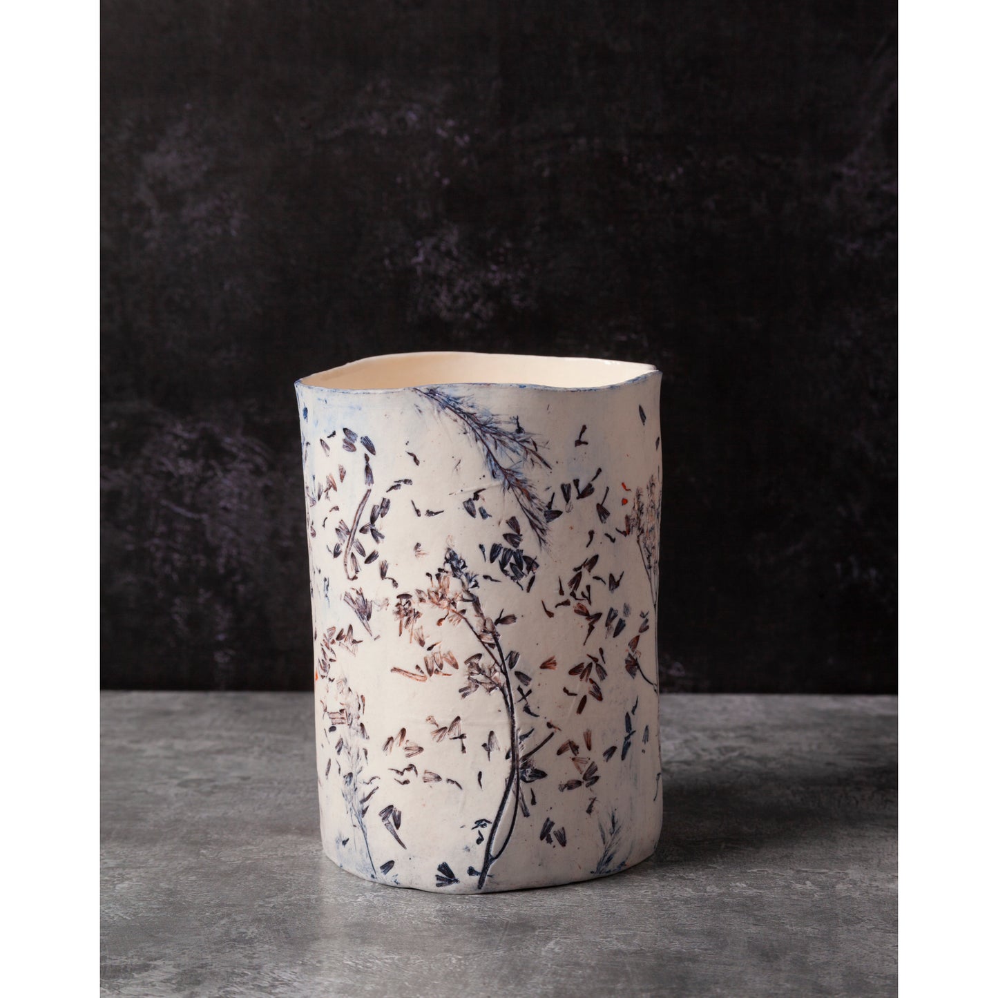 Ceramic vessel with lavender, grasses and leaf patterns on a white porcelain surface. High lights of blue and orange