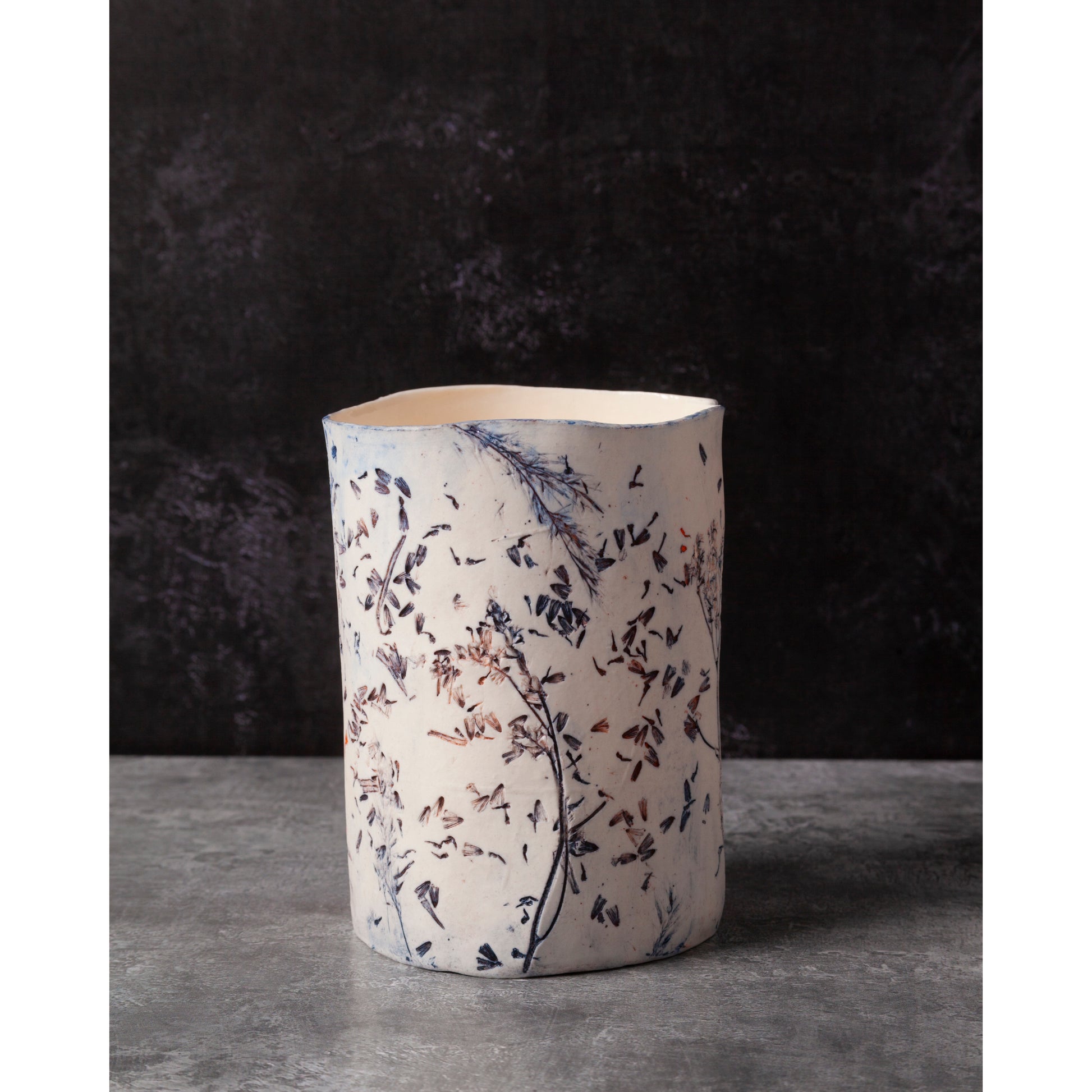 Ceramic vessel with lavender, grasses and leaf patterns on a white porcelain surface. High lights of blue and orange