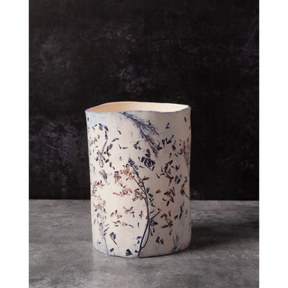 Ceramic vessel with lavender, grasses and leaf patterns on a white porcelain surface. High lights of blue and orange