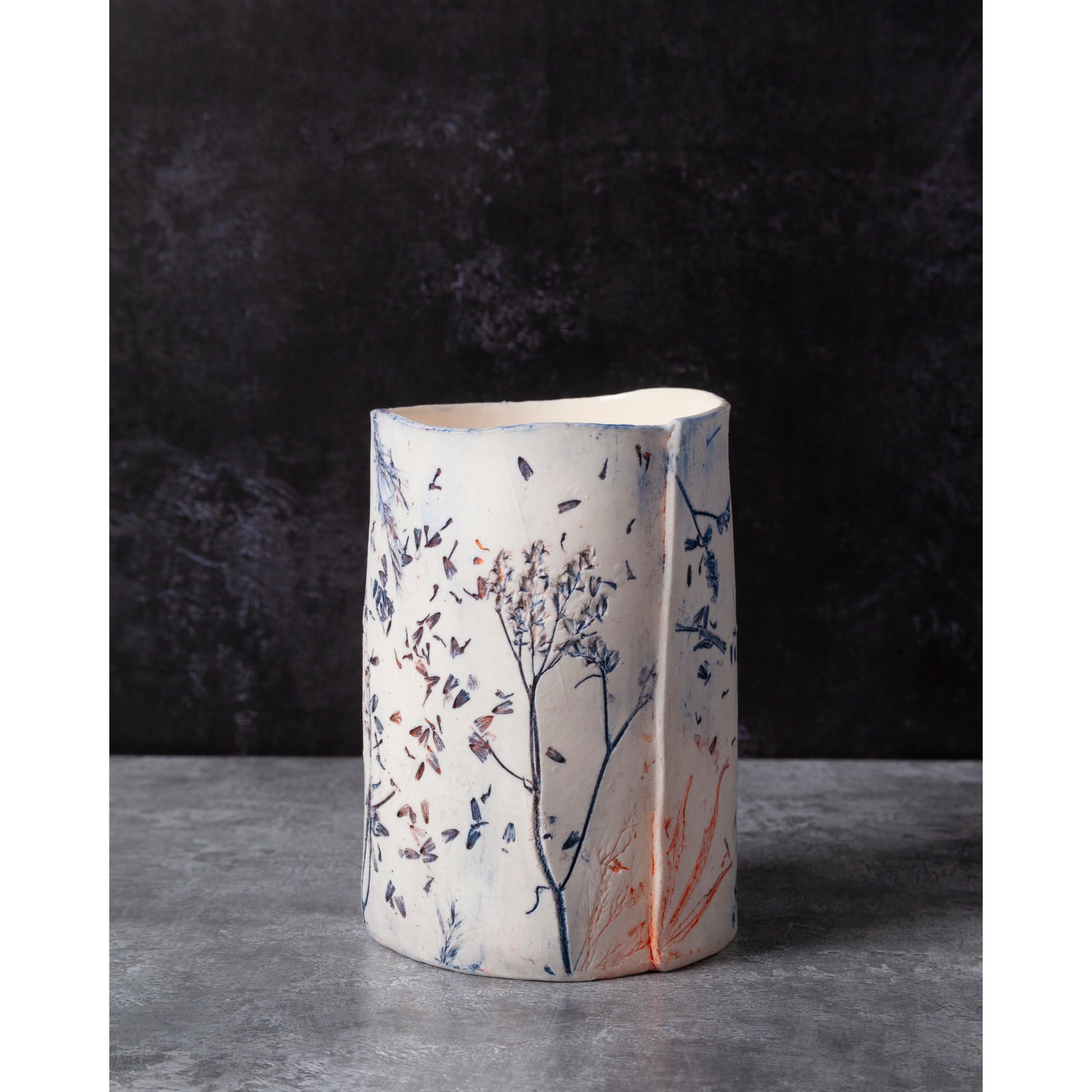 Ceramic vessel with lavender, grasses and leaf patterns on a white porcelain surface. High lights of blue and orange