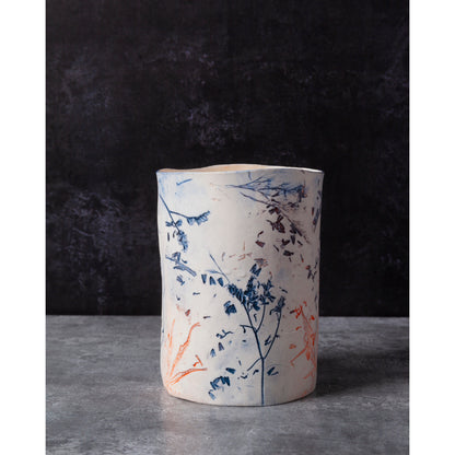Ceramic vessel with lavender, grasses and leaf patterns on a white porcelain surface. High lights of blue and orange