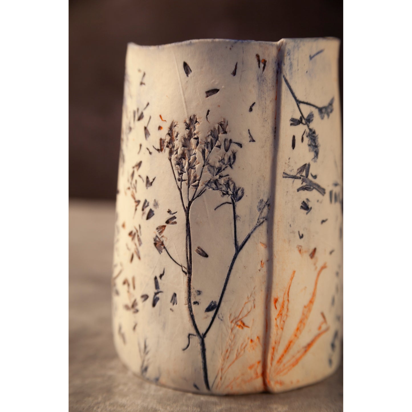 Ceramic vessel with lavender, grasses and leaf patterns on a white porcelain surface. High lights of blue and orange