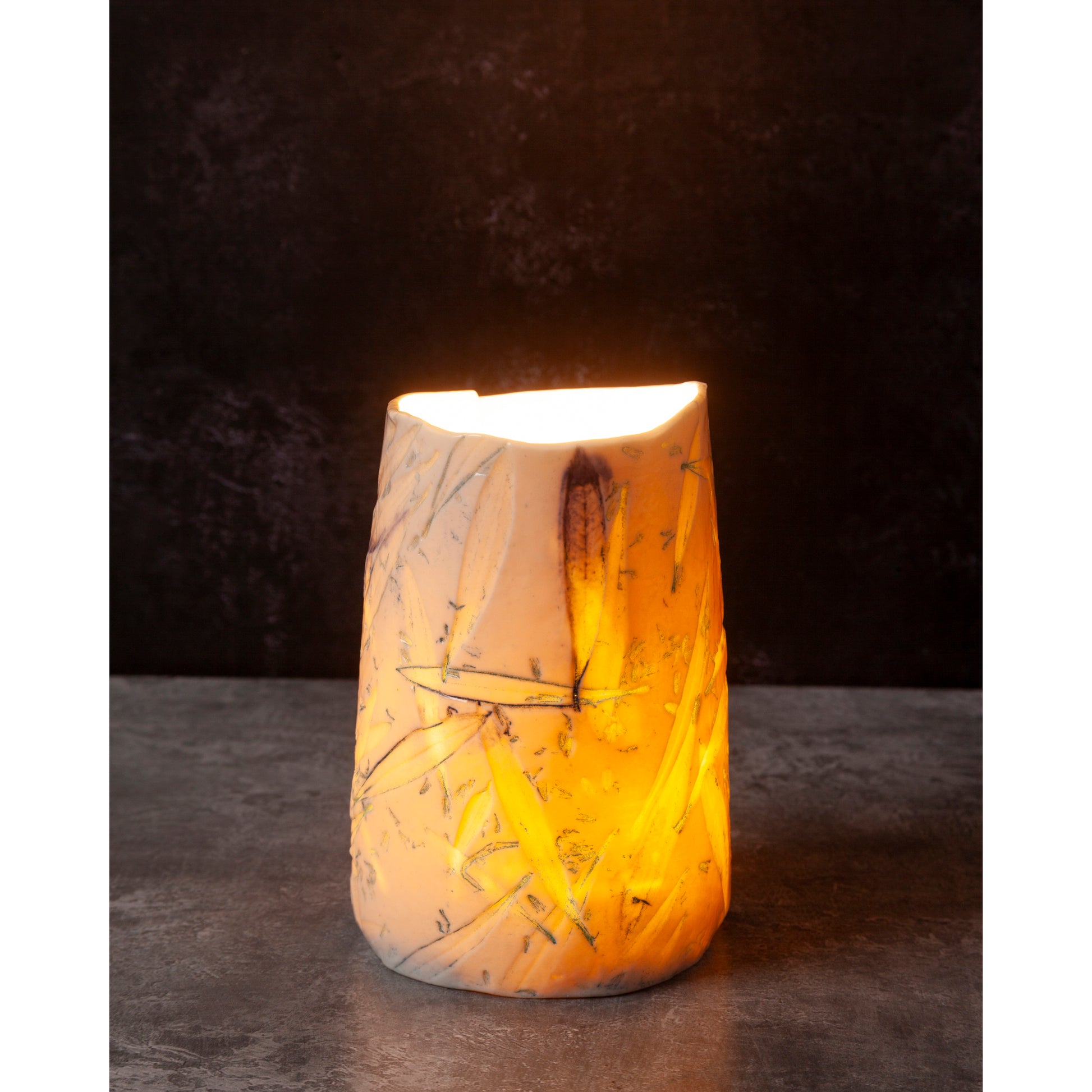 Ceramic night light / vase with blue abstract patterns using olive leaves and lavender seeds glowing softly against a dark background.