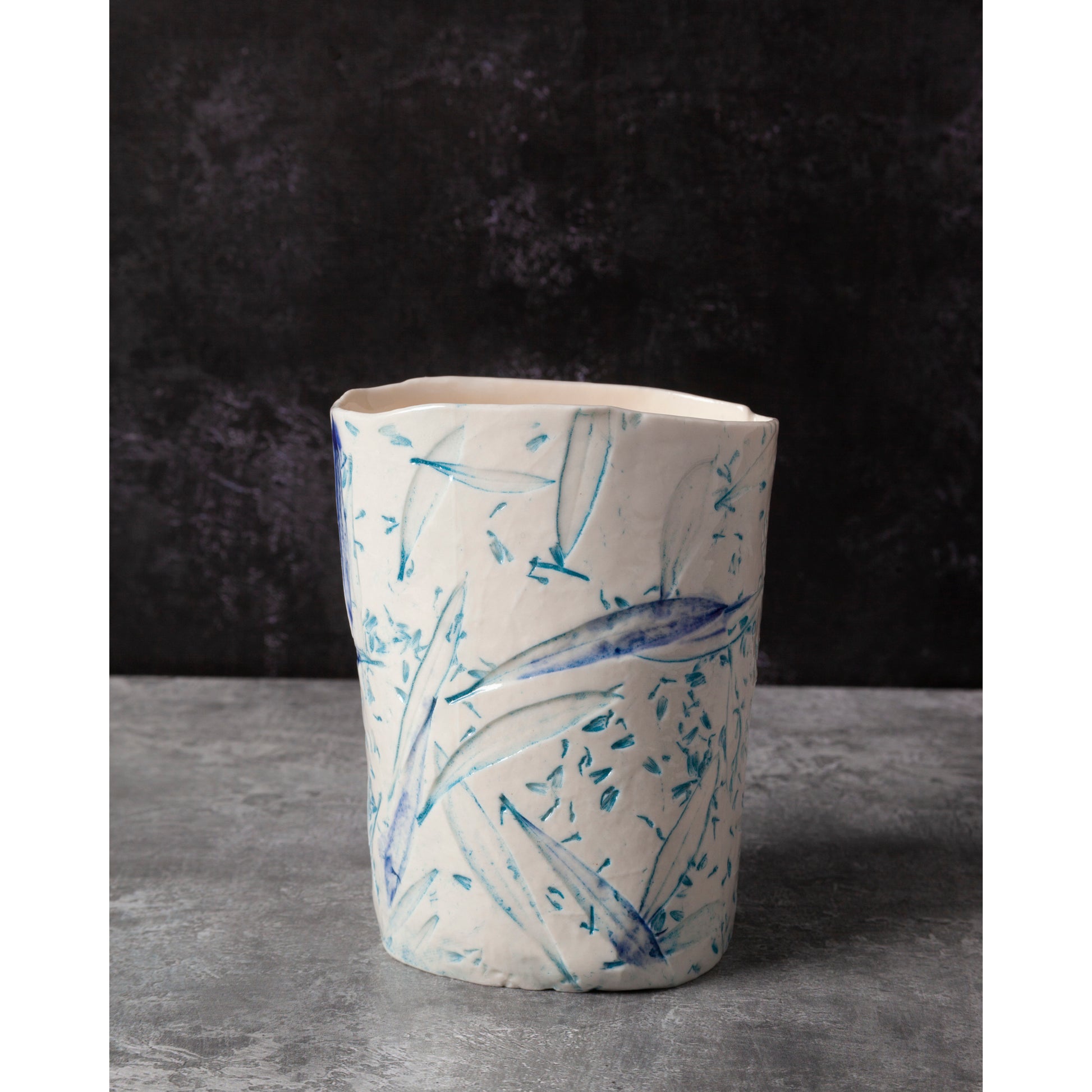 Ceramic night light / vase with blue abstract patterns using olive leaves and lavender seeds against a dark background.