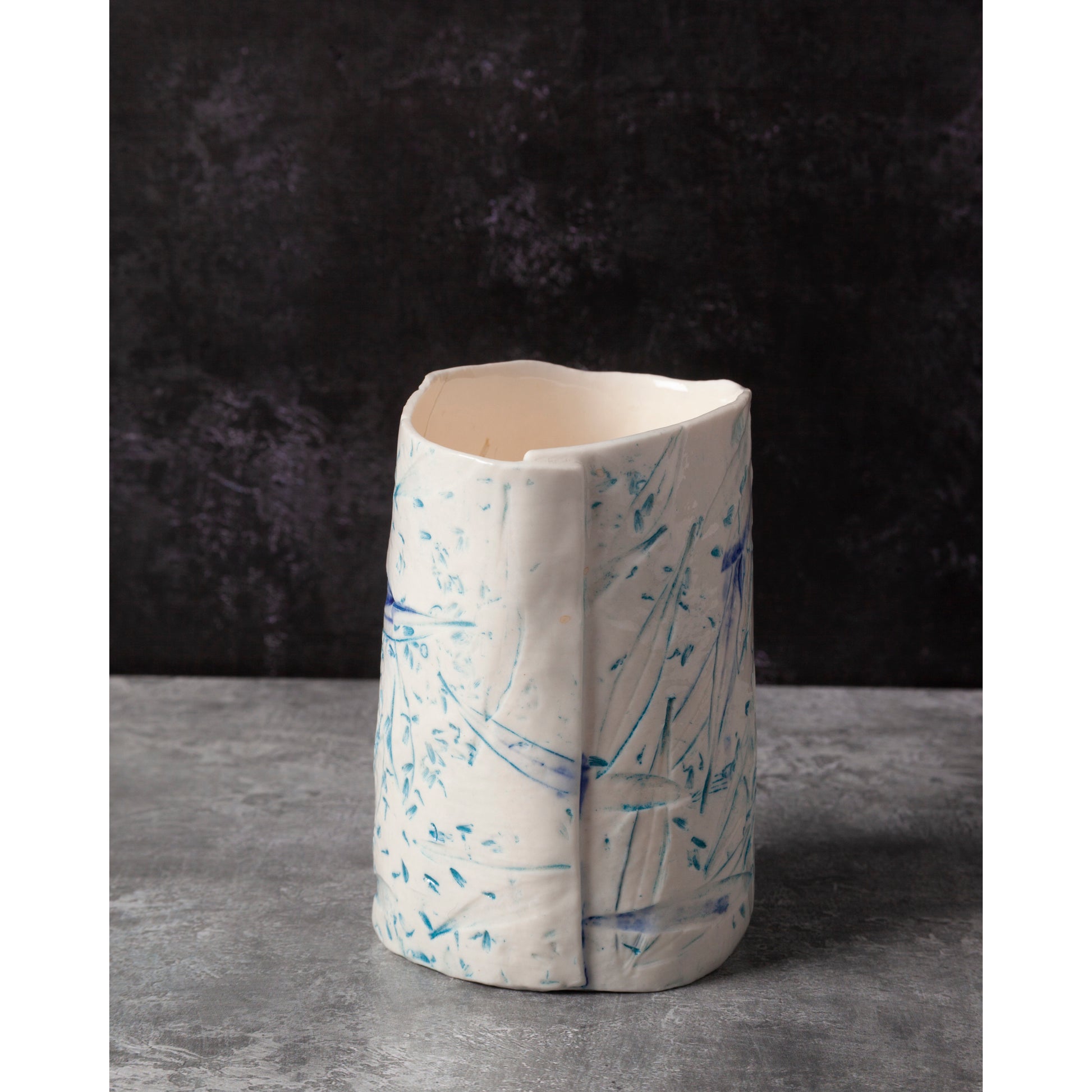 Ceramic night light / vase with blue abstract patterns using olive leaves and lavender seeds against a dark background.