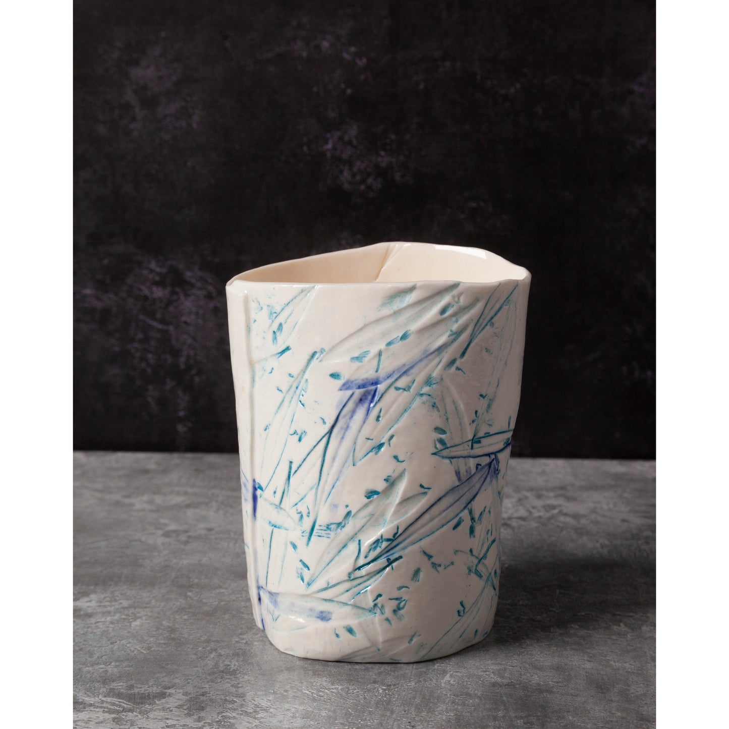 Ceramic night light / vase with blue abstract patterns using olive leaves and lavender seeds against a dark background.
