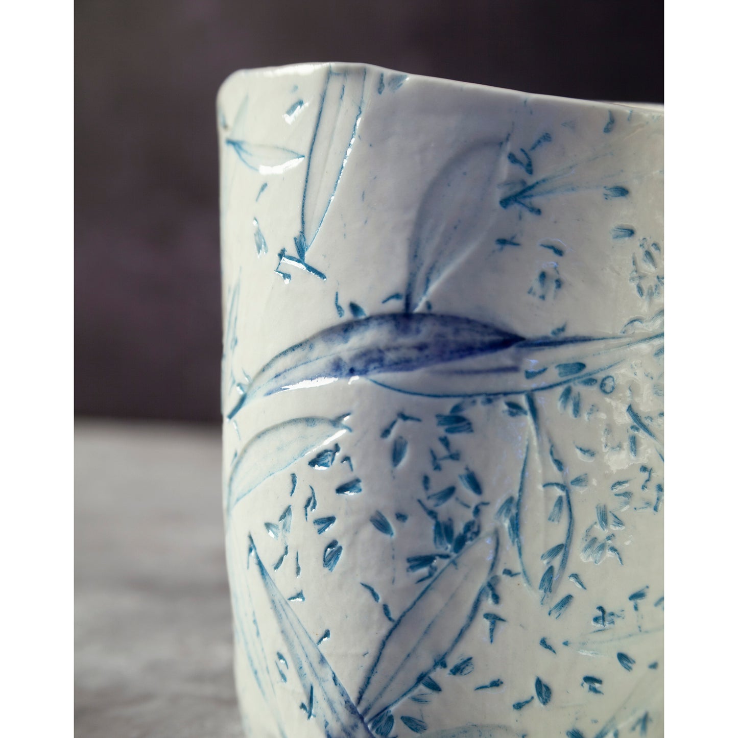 Close up of ceramic night light / vase with blue abstract patterns using olive leaves and lavender seeds against a dark background.