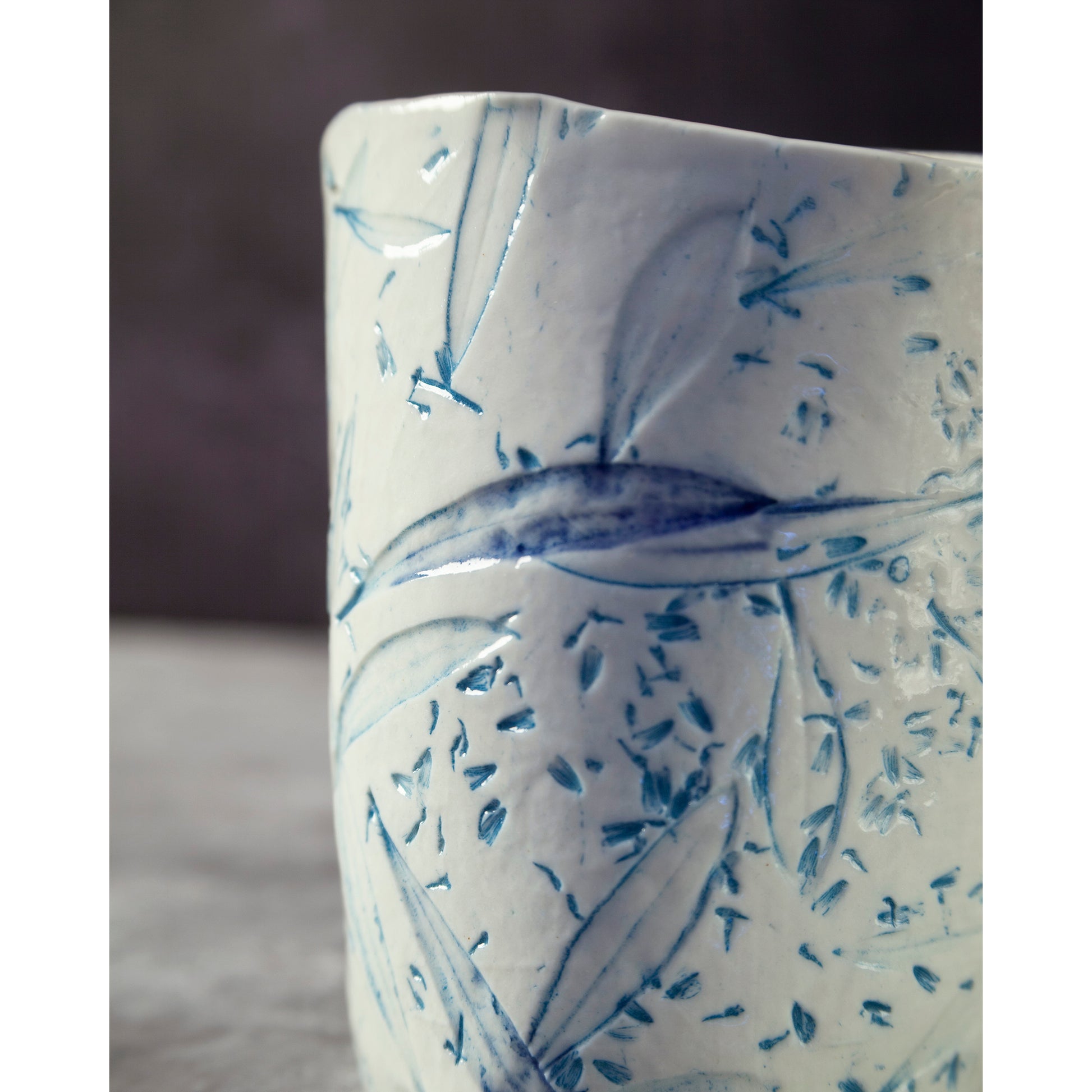 Close up of ceramic night light / vase with blue abstract patterns using olive leaves and lavender seeds against a dark background.