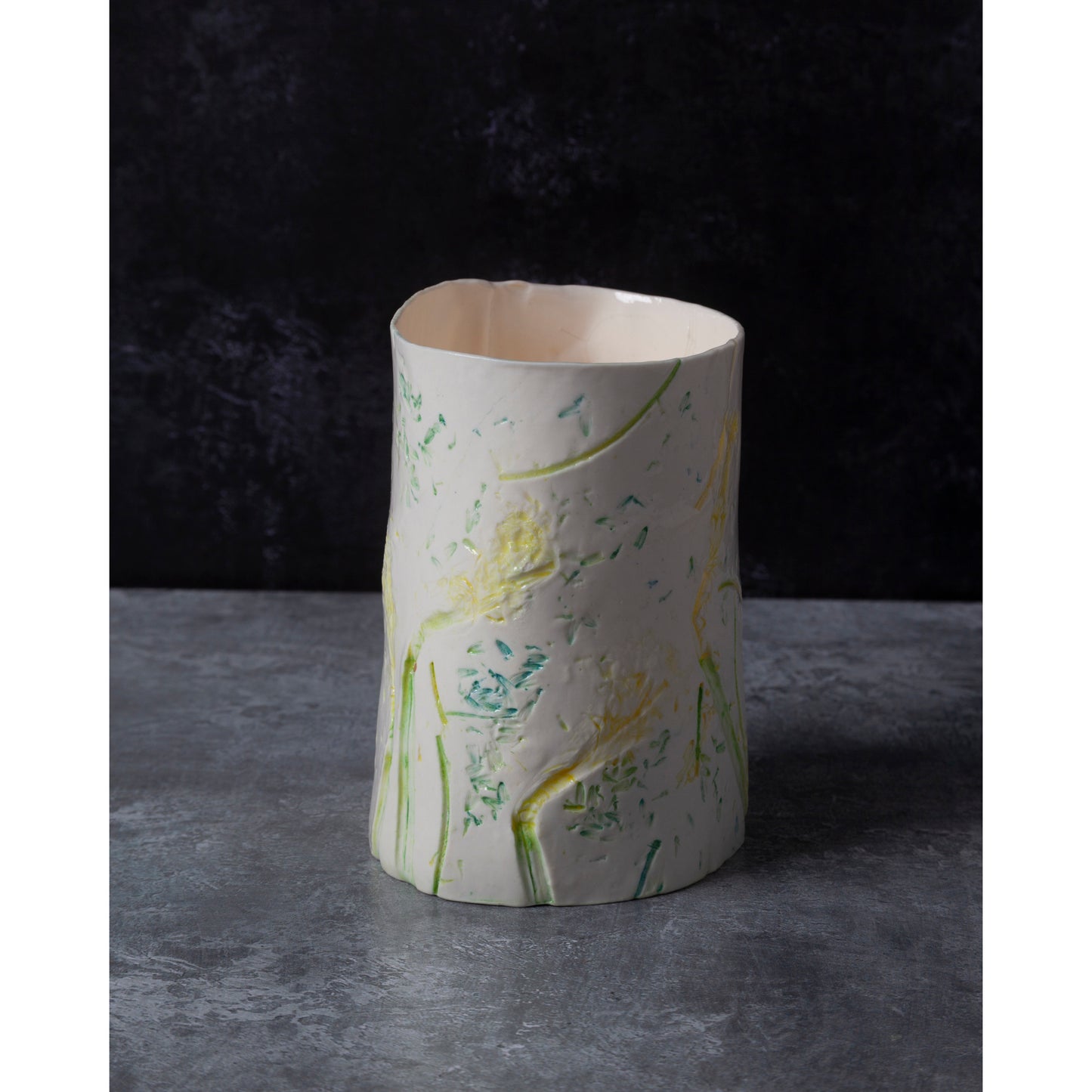 Cylindrical porcelain ceramic vase with artistic daffodil design. photographed against a dark background