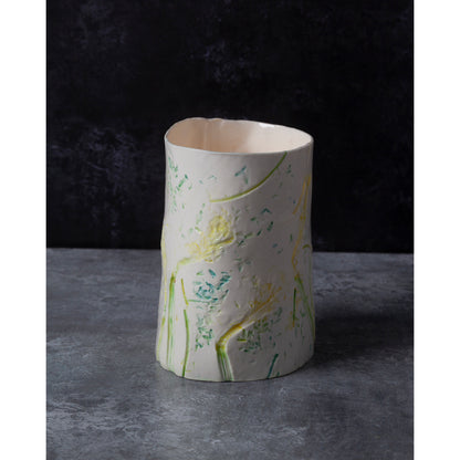 Cylindrical porcelain ceramic vase with artistic daffodil design. photographed against a dark background