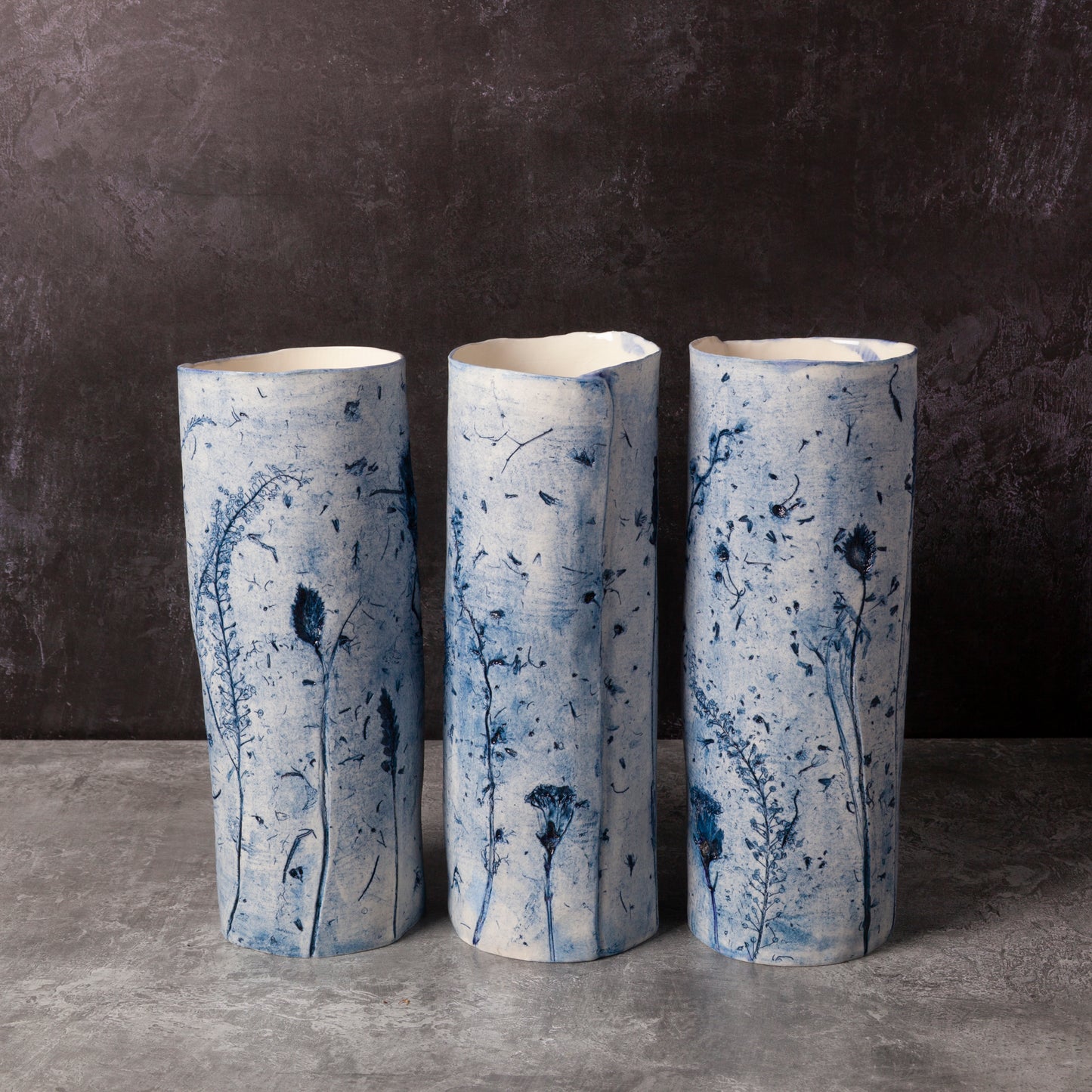 Three cylindrical ceramic vases with blue floral patterns on a dark background