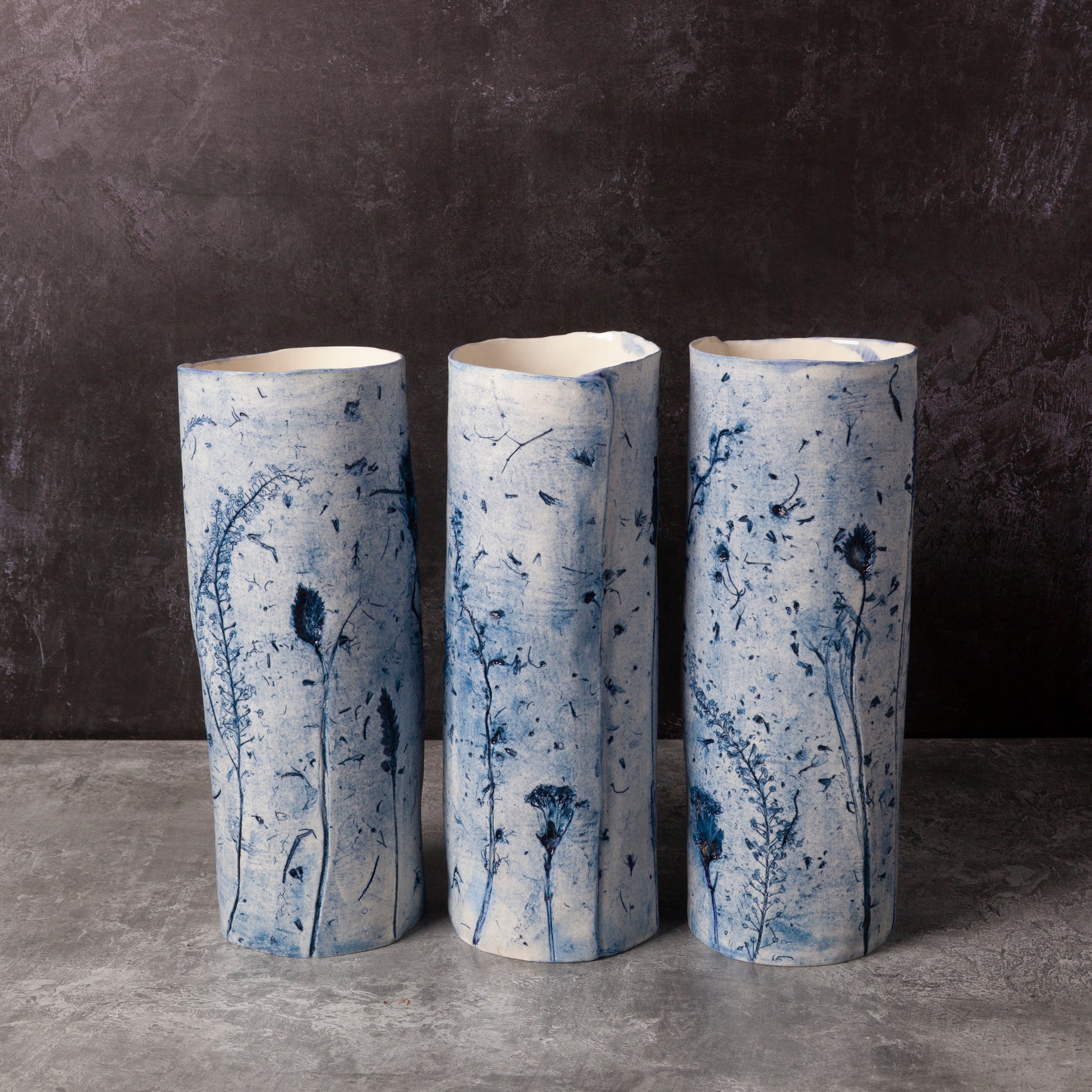 Three cylindrical ceramic vases with blue floral patterns on a dark background