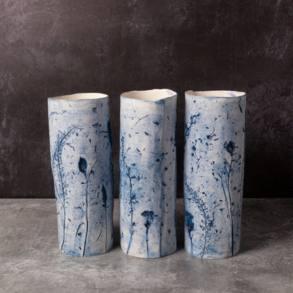 Three cylindrical ceramic vases with blue floral patterns on a dark background