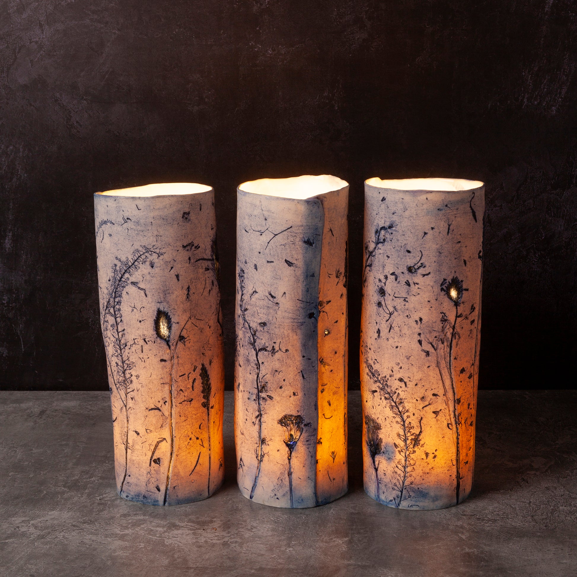 Three cylindrical porcelain night light vases with natural patterns on a dark background